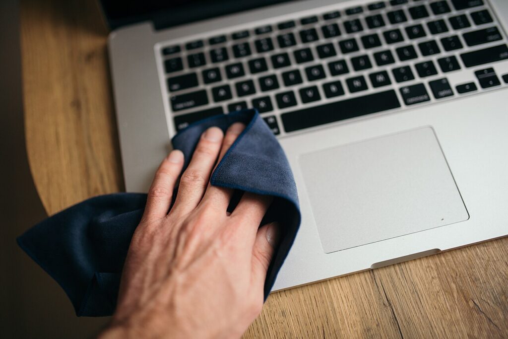 A person cleaning a laptop with a cloth