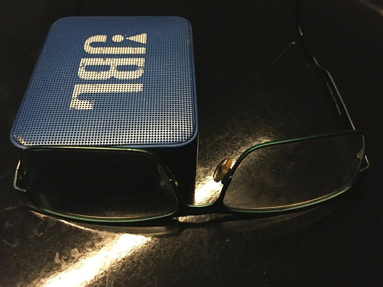 portable Bluetooth speaker next to glasses showing its small size